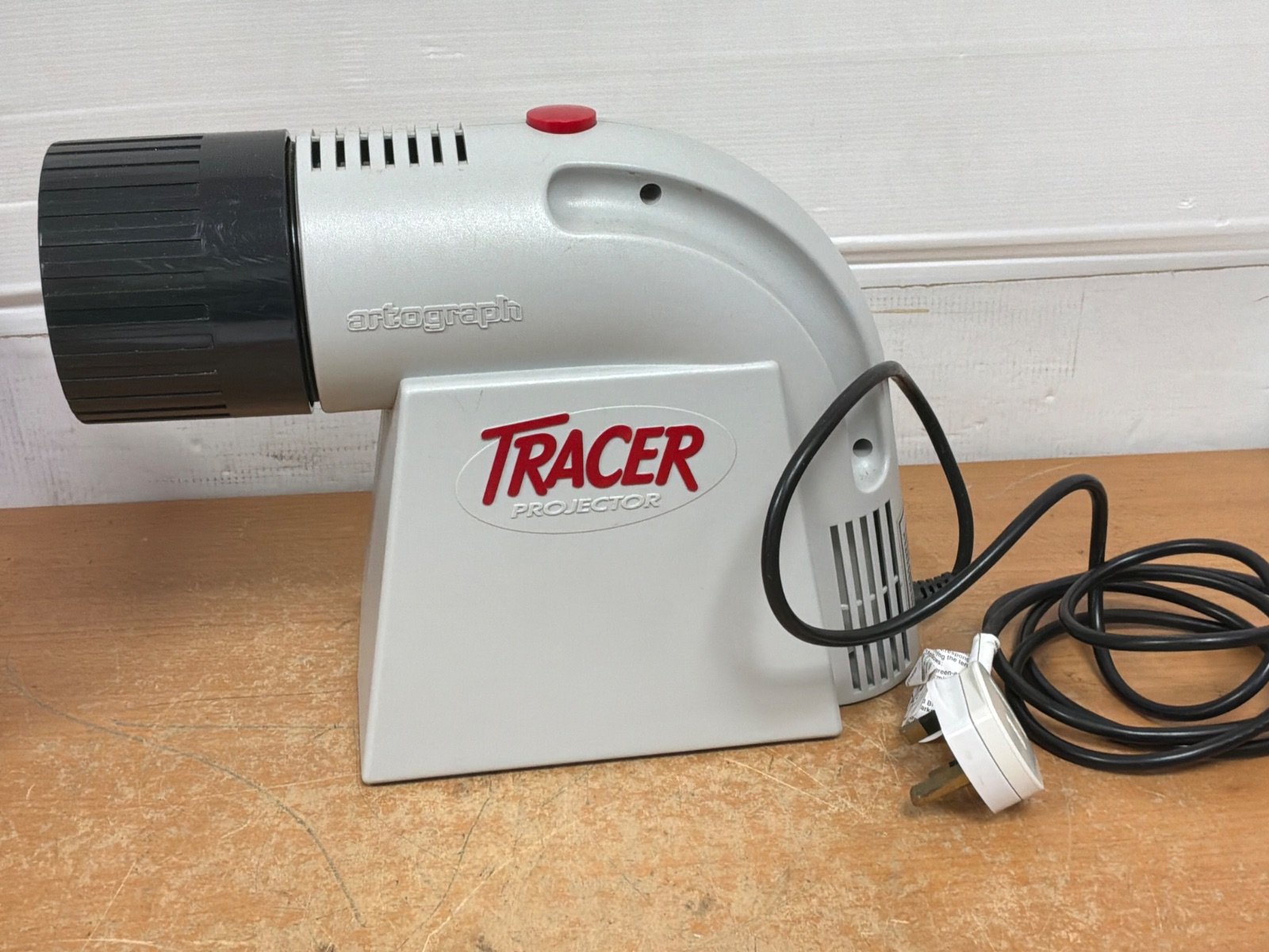 A grey Tracer projector lamp with a black lens, in good condition, featuring a power cord and a red button on the side.